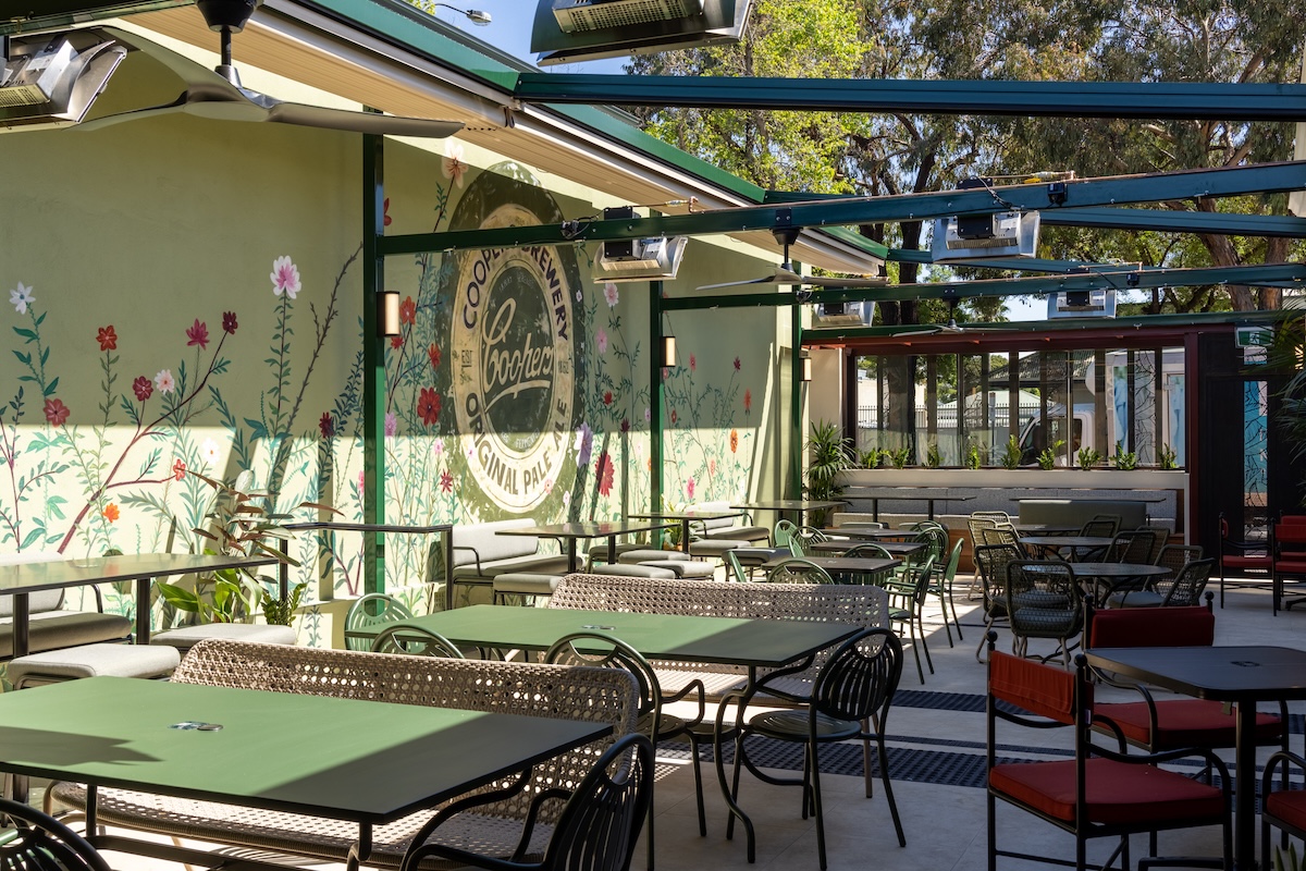 The Colonist outdoor beer garden with green dining tables, overhead heaters, and a Coopers Brewery floral wall mural.